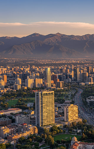 Vista aérea de Santiago de Chile al atardecer, con edificios, cordillera de los Andes y autopista.