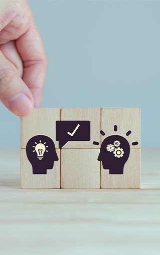 Mano colocando bloque de madera con ícono de cabeza, ampolleta e ideas, simbolizando el proceso de asesoría y soluciones estratégicas.